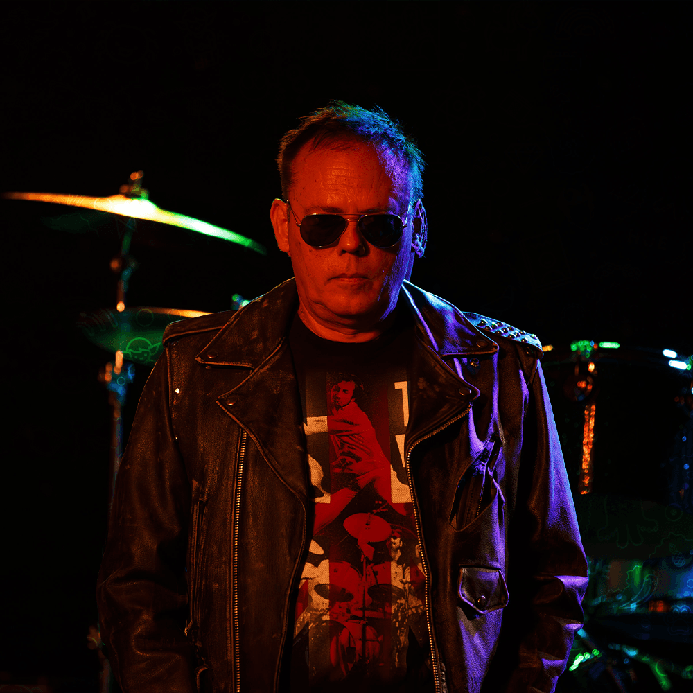 Lynn Cude in a leather jacket and sunglasses on a dark stage